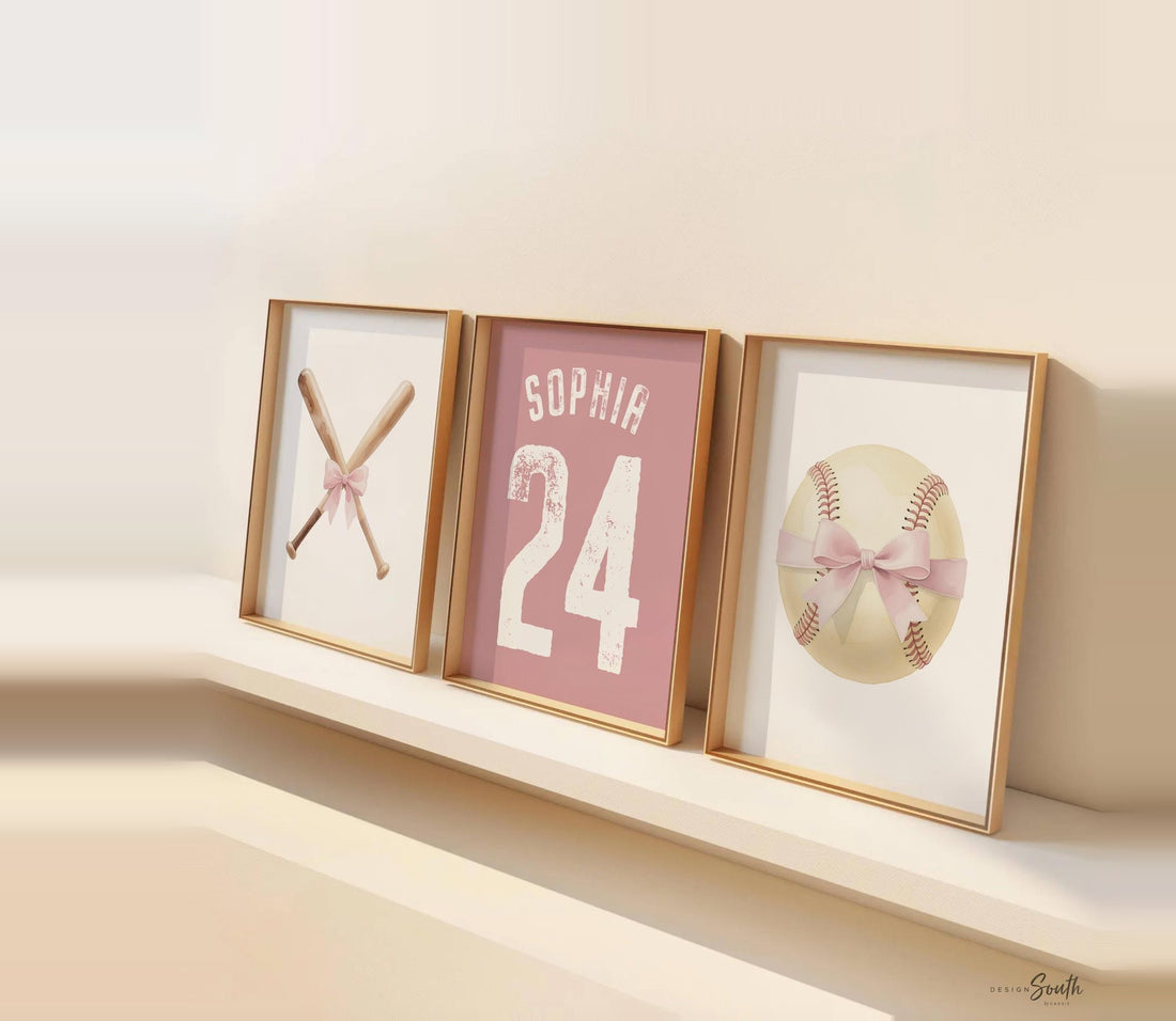 Three framed baseball nursery prints on a cream shelf: crossed bats with a bow, a personalized jersey print reading Sophia 24, and a baseball tied with a bow.