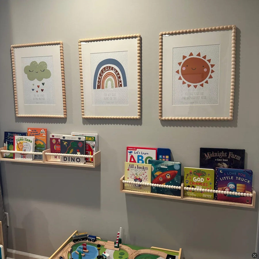 Customer photo of Design South cloud, rainbow, and sun prints in beaded frames above book ledges in a playroom.