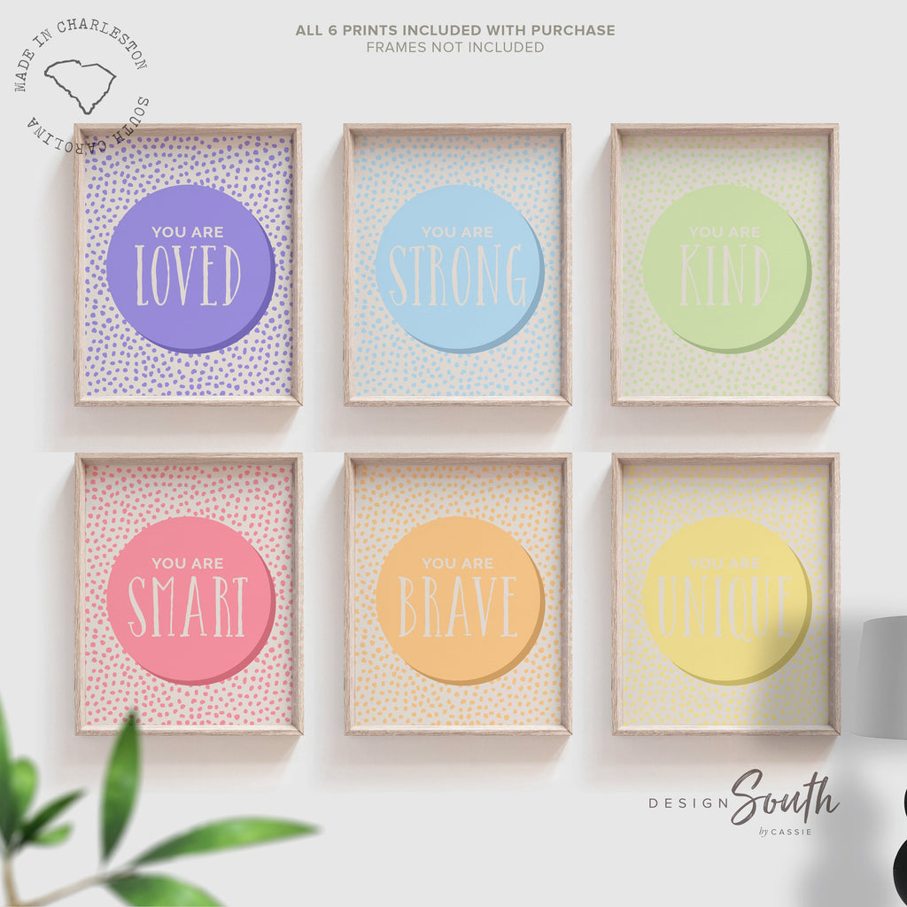 Set of 6 inspirational wall art prints for kids featuring rainbow-colored circles with modern speckled designs. Each print includes a positive affirmation: you are loved, you are kind, you are brave, you are smart, you are strong. Designed in purple, blue, green, pink, orange, and yellow for a vibrant and trendy playroom or nursery. This uplifting art set is perfect for encouraging confidence and positivity in babies, toddlers, or young children’s spaces.