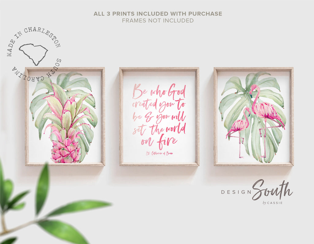 May include: Three framed prints with a tropical theme. The prints feature pink flamingos, green monstera leaves, and a pink pineapple. The center print has a pink quote that reads &#39;Be who God created you to be & you will set the world on fire.&#39; The quote is attributed to St. Catherine of Siena.