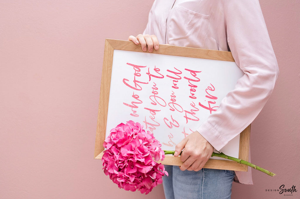 May include: Three framed prints with a tropical theme. The prints feature pink flamingos, green monstera leaves, and a pink pineapple. The center print has a pink quote that reads &#39;Be who God created you to be & you will set the world on fire.&#39; The quote is attributed to St. Catherine of Siena.