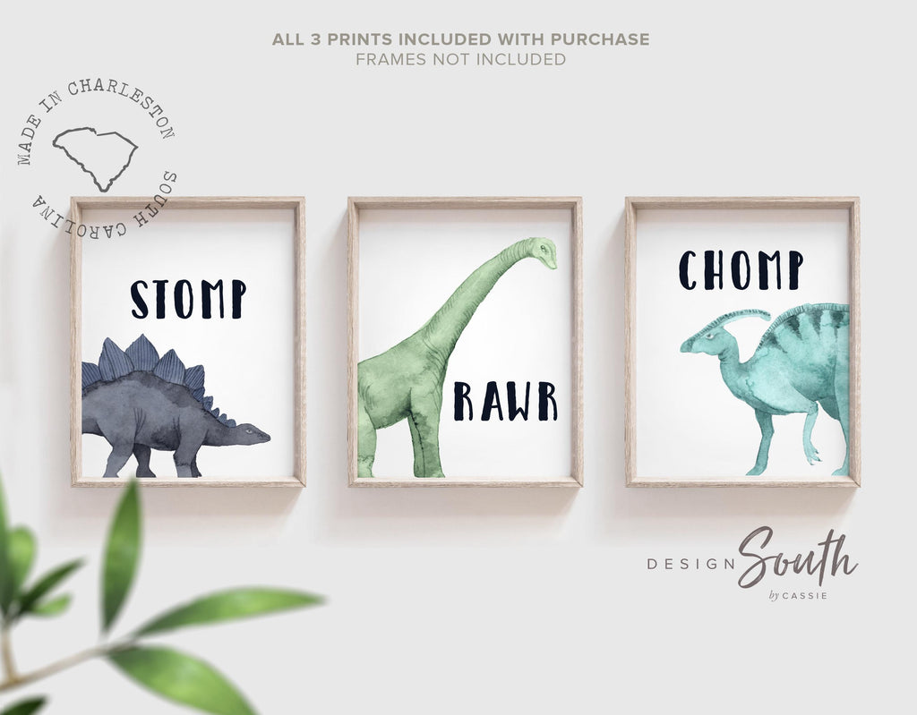 Watercolor dinosaur wall art set of 3 featuring a brachiosaurus, stegosaurus, and parasaurolophus in navy blue, green, and teal tones. Each print includes fun dinosaur-themed words: “Stomp,” “Roar,” and “Chomp,” making it perfect for a kids’ bedroom, playroom, or dinosaur-themed nursery. This playful and colorful artwork set adds a whimsical, prehistoric touch to any child’s space and makes a great gift for dino-loving toddlers or new parents decorating a gender-neutral nursery. by Design South.