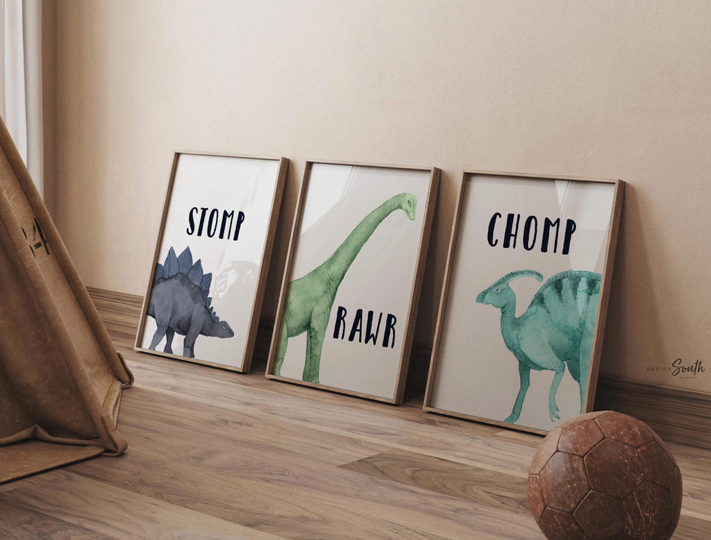 Watercolor dinosaur wall art set of 3 featuring a brachiosaurus, stegosaurus, and parasaurolophus in navy blue, green, and teal tones. Each print includes fun dinosaur-themed words: “Stomp,” “Roar,” and “Chomp,” making it perfect for a kids’ bedroom, playroom, or dinosaur-themed nursery. This playful and colorful artwork set adds a whimsical, prehistoric touch to any child’s space and makes a great gift for dino-loving toddlers or new parents decorating a gender-neutral nursery. by Design South.