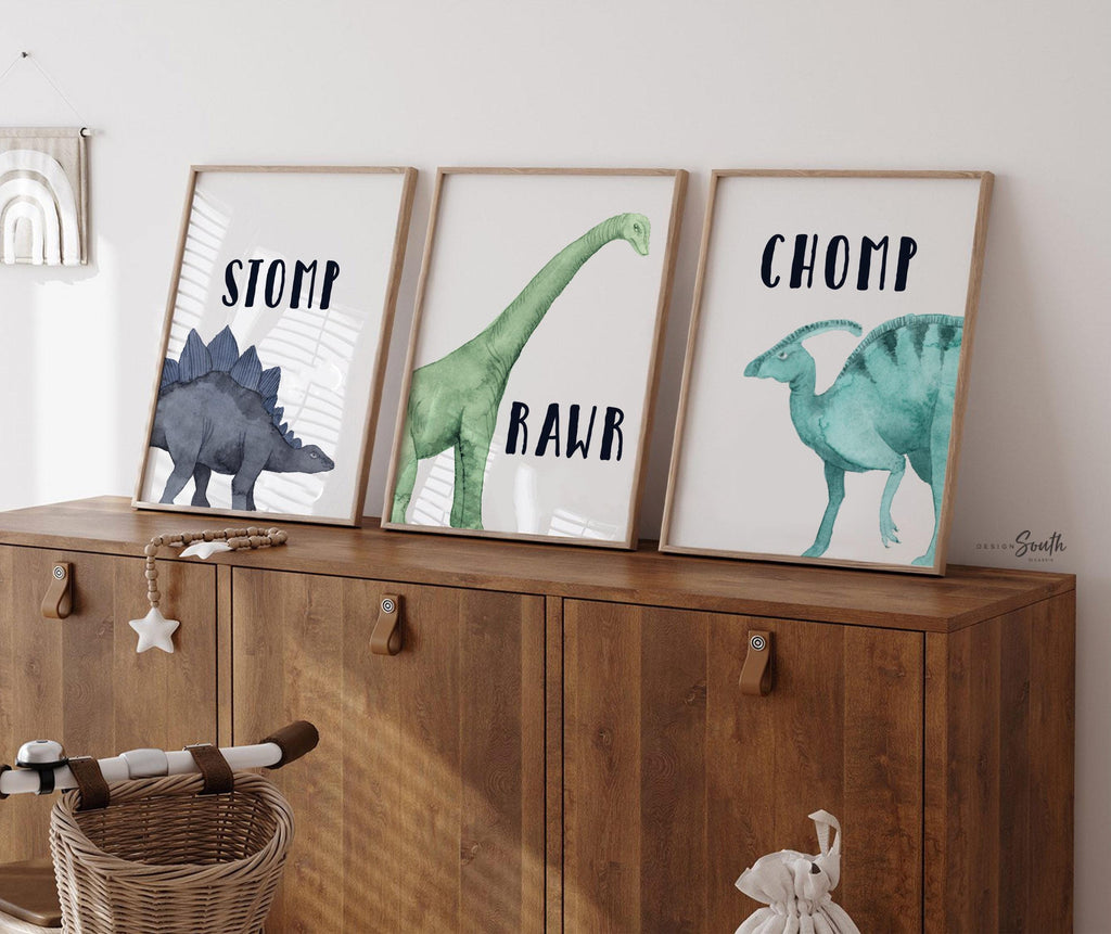 Watercolor dinosaur wall art set of 3 featuring a brachiosaurus, stegosaurus, and parasaurolophus in navy blue, green, and teal tones. Each print includes fun dinosaur-themed words: “Stomp,” “Roar,” and “Chomp,” making it perfect for a kids’ bedroom, playroom, or dinosaur-themed nursery. This playful and colorful artwork set adds a whimsical, prehistoric touch to any child’s space and makes a great gift for dino-loving toddlers or new parents decorating a gender-neutral nursery.