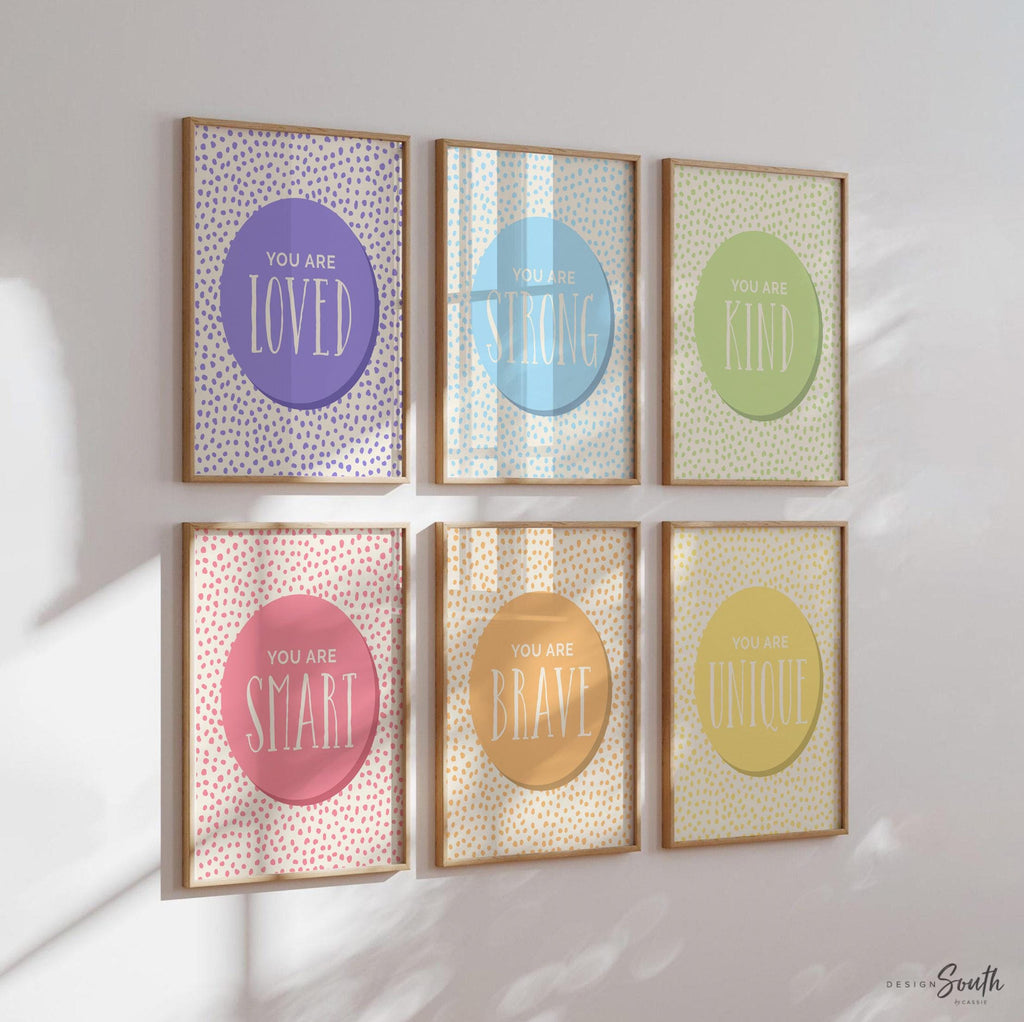 Set of 6 inspirational wall art prints for kids featuring rainbow-colored circles with modern speckled designs. Each print includes a positive affirmation: you are loved, you are kind, you are brave, you are smart, you are strong. Designed in purple, blue, green, pink, orange, and yellow for a vibrant and trendy playroom or nursery. This uplifting art set is perfect for encouraging confidence and positivity in babies, toddlers, or young children’s spaces.