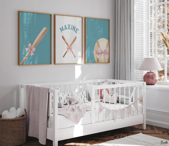 May include: Three framed baseball-themed prints with a teal background. One print features a baseball bat with a pink bow, another has crossed bats, and the third shows a baseball with a pink bow. The prints are above a white crib.